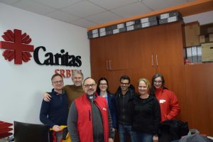 Delatnici Caritasa Srbije i Caritasa Austrije ispred  Velikog Caritasovog logotipa na zidu u kancelariji Caritasa Srbije