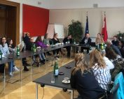 Svi učesnici sede zajedno za stolom. U pozadini je zastava Austrije i Evropske unije