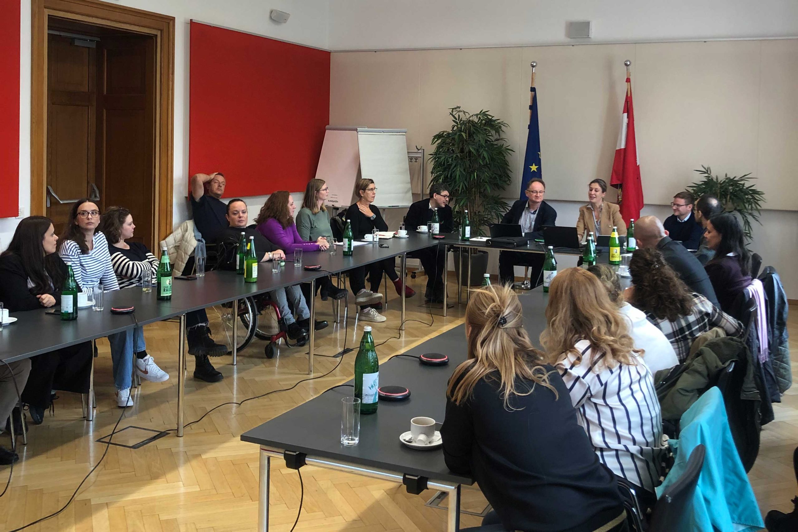 Svi učesnici sede zajedno za stolom. U pozadini je zastava Austrije i Evropske unije