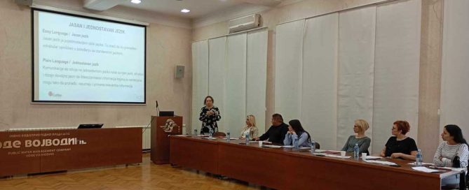 Anita Govlja, Caritas Srbije drži predavanje učesnicima obuke. Pet ljudi sedi za stolom.