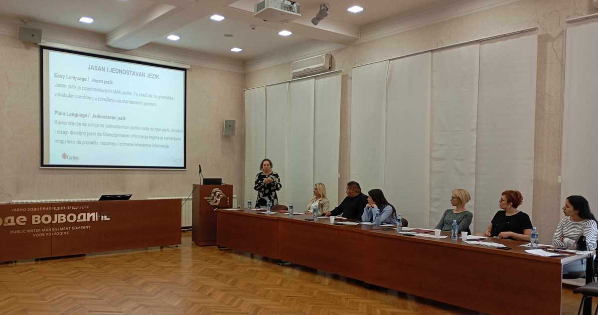 Anita Govlja, Caritas Srbije drži predavanje učesnicima obuke. Pet ljudi sedi za stolom.